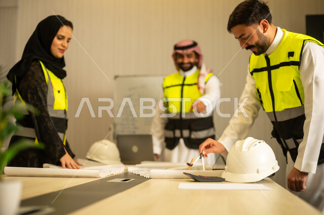 مناقشة مخطط البناء، التعاون المهني داخل المكتب الهندسي، متابعة سير المشروع، مفهوم التخطيط والتنظيم، مهندس عربي خليجي سعودي يرتدي الشماغ و سترة السلامة يقف برفقة زملائه يقوم بشرح العمل