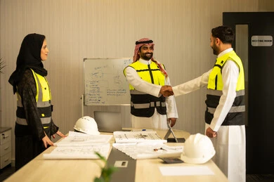 تصميم وتخطيط المخططات المعمارية، إيماءات السعادة والسرور، الشركات المختصة بورشات البناء والمقاولات، مهندسان عربيان خليجيان سعوديان يرتديان الثوب التقليدي و سترة الحماية يقومان بالمصافحة، عقد اتفاقيات عمل جديدة