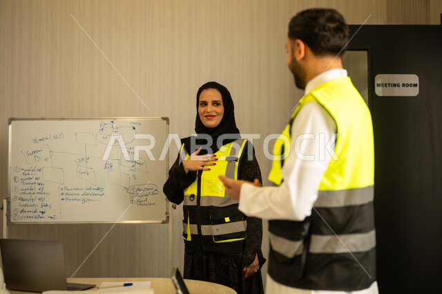 ادارة المشاريع الهندسية والانشاءات، دراسة المخطط والمشروع ، مهنة ووظيفة هندسية، مهندس عربي خليجي سعودي يرتدي الثوب و سترة الحماية يقوم بالتحدث مع زميلته