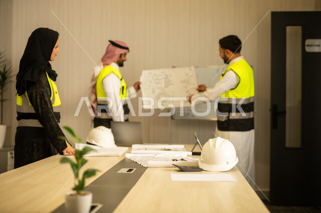 Studying the plan and project, a profession and engineering job for youth, monitoring and following up on construction processes, the concept of managing engineering projects and constructions, two Arab Gulf engineers from Saudi Arabia wearing white thobes and safety vests carrying the engineering plan accompanied by their colleague.