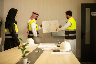 Studying the plan and project, a profession and engineering job for youth, monitoring and following up on construction processes, the concept of managing engineering projects and constructions, two Arab Gulf engineers from Saudi Arabia wearing white thobes and safety vests carrying the engineering plan accompanied by their colleague.