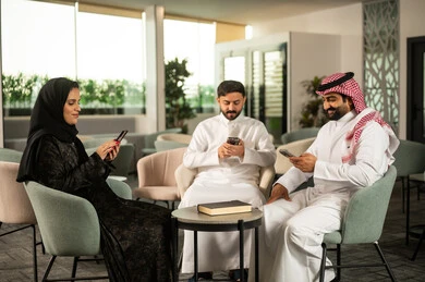 مفهوم استخدام الأجهزة الذكية في بيئة العمل, التواصل الرقمي وتبادل المعلومات, مجموعة من الموظفين العرب الخليجيين السعوديين يرتدون الزي التقليدي يستخدمون الهاتف المحمول، ايماءات الاندماج و التركيز