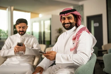 Browsing social media sites on the internet, communicating and chatting with friends and relatives via mobile, using a modern and advanced technical device, two Arab Gulf men from Saudi Arabia wearing traditional attire are using a mobile phone.