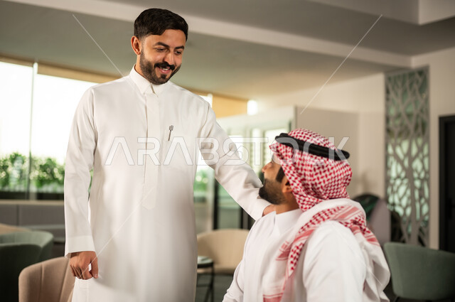 اكتساب الخبرة وتوسيع شبكة العلاقات المهنية، رجل عربي خليجي سعودي يرتدي الثوب الابيض يقوم بالتحدث مع زميلة، التعاون و العمل الجماعي، توجيه الجهود لتحقيق أهداف الشركة