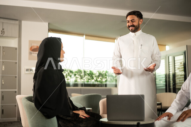 التواصل الفعال وتنسيق المهام اليومية, موظف عربي خليجي سعودي  يرتدي الثوب الابيض يقوم بشرح المهام لزميلته ، مناقشة الأفكار وتبادل الآراء، العمل الجماعي والتواصل المهني
