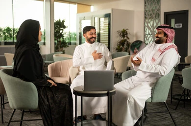 مفهوم العمل الجماعي و التواصل والتعاون المهني, تبادل الأفكار ومناقشة المهام اليومية, موظفة عربية خليجية سعودية ترتدي العباءة والحجاب تشارك في الحوار مع زملائها ، ايماءات السعادة و السرور