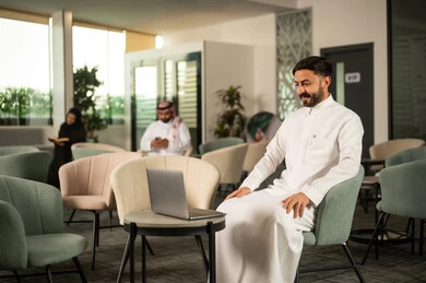 اجراء مكالمة فيديو ، إنجاز العمل اونلاين من خلال الحاسب المحمول، رجل عربي خليجي سعودي يرتدي الثوب الابيض يجلس على كرسي امام الابتوب، تطور التكنولوجيا وإستخدام الأجهزة التقنية الحديثة