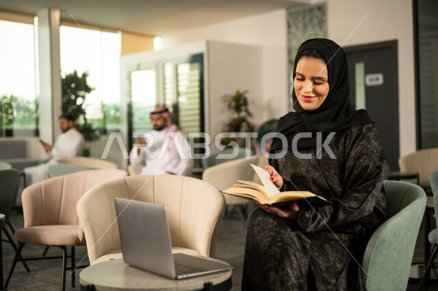 مفهوم الشغف بالقراءة، تنمية وتعزيز المعلومات العامة, الجمع بين القراءة والتقنية في العمل اليومي, امراة عربية خليجية سعودية تجلس امام الحاسب المحمول و تقوم بقراءة كتاب، ثقافة التعلم الذاتي