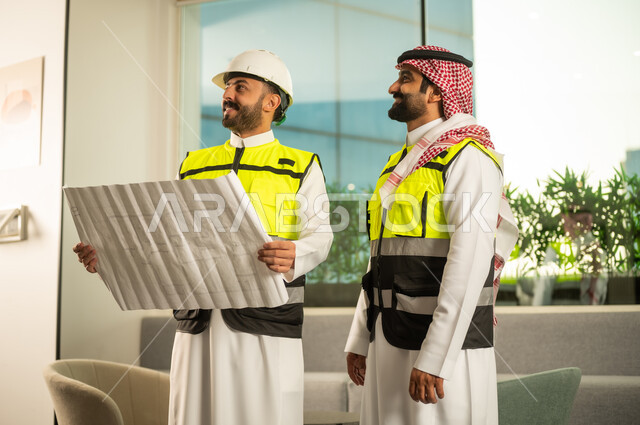 النظر الى شي ما فى الاعلى، متابعة تنفيذ الخطط الهندسية، الشركات المختصة بورشات البناء والمقاولات، التخطيط ووضع اساسيات المخططات المعمارية، مهندسان عربيان خليجيان سعوديان يرتديان سترة الحماية يعملان على مناقشة مخطط الإنشاء وتحديد القياسات بدقة