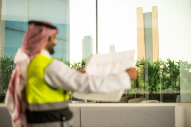 Engineering project management and construction, the concept of studying the plan and construction project, a profession and engineering job for youth, a Saudi Gulf Arab engineer wearing traditional attire and a safety vest working in the engineering sector in the Kingdom of Saudi Arabia reviewing the engineering plan.