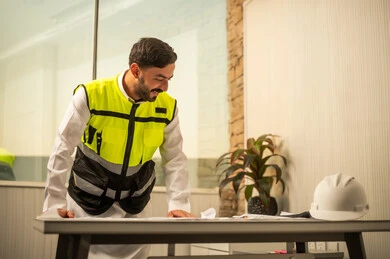 مفهوم الإدارة الهندسية والتخطيط المسبق، الدقة المهنية والعمل الهندسي، مهندس عربي خليجي سعودي يرتدي الثوب و سترة الحماية يعمل على مراجعة التصاميم الهندسية داخل بيئة مكتبية حديثة