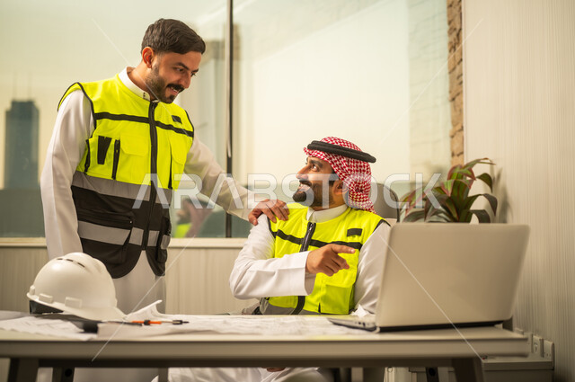Engineering project management, the concept of teamwork among engineers, the use of technology in engineering planning, a Saudi Gulf Arab engineer wearing a ghutrah and safety vest working on a laptop alongside a colleague.