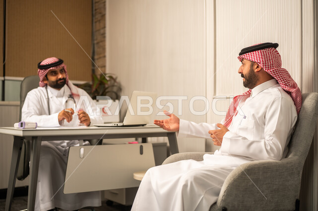 Working in the healthcare sector, the concept of medical consultation in the medical center, an Arab Gulf Saudi doctor wearing a white thobe, a ghutrah, and a lab coat sitting behind the desk and listening to the patient.