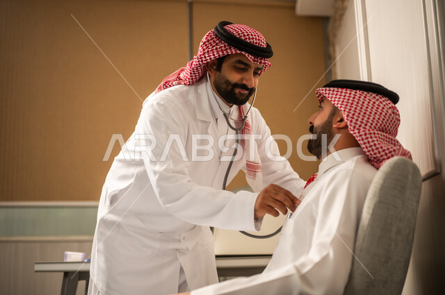 العمل في القطاع الصحي، طبيب عربي خليجي سعودي يرتدي الثوب الابيض و الشماغ و المعطف الطبي يقوم باستخدام سماعه الفحص الطبية للمريض، المتابعة الدورية لفحص نبضات القلب، مفهوم الطب والرعاية الصحية، قياس معدل ضربات القلب