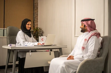 A medical consultation session inside a clinic, the concept of communication between the doctor and the patient, modern healthcare, an Arab Gulf Saudi female doctor wearing a white coat and a hijab using a laptop, discussing the patient's health condition.