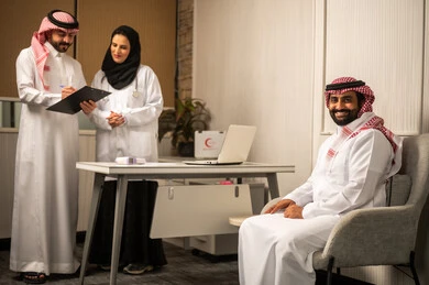 The concept of medicine and healthcare, medical consultation within the clinic, regular medical follow-up for the patient, an Arab Gulf doctor and doctor from Saudi Arabia wearing medical attire reviewing the medical file, looking at the camera with expressions of happiness and joy, writing and taking notes.