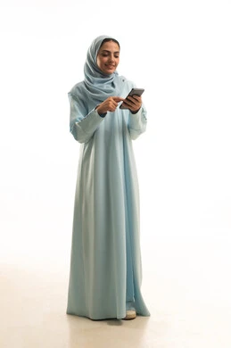Chatting with family and friends and browsing social media, using modern technological devices, a portrait of a Saudi Gulf Arab woman wearing an abaya and hijab holding a mobile phone, gestures of happiness and joy, full-body, white background.