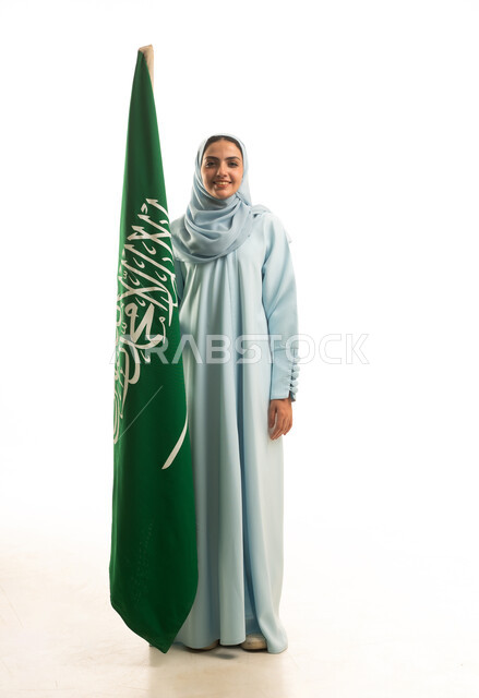 ذكرى يوم بدينا 1727 م، مفهوم حب الوطن و الانتماء اليه، الاحتفال بتأسيس الدولة السعودية الأولى 22 فبراير، يوم العلم السعودي11 مارس، بورتريه لإمرأة عربية خليجية سعودية ترتدي العباءة و الحجاب تمسك راية وشعار المملكة بايماءات الاعتزاز و الفخر, الجسم بالطول الكامل, خلفية بيضاء