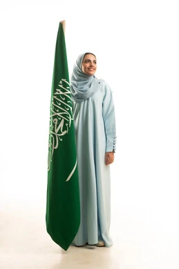 مفهوم حب الوطن و الانتماء اليه، الاحتفال بتأسيس الدولة السعودية الأولى 22 فبراير، يوم العلم السعودي11 مارس، ذكرى يوم بدينا 1727 م، بورتريه لإمرأة عربية خليجية سعودية ترتدي العباءة و الحجاب تمسك راية وشعار المملكة بايماءات الاعتزاز و الفخر, الجسم بالطول الكامل, خلفية بيضاء