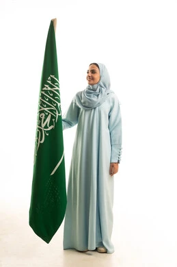 الاحتفال بتأسيس الدولة السعودية الأولى 22 فبراير، مفهوم حب الوطن و الانتماء اليه، يوم العلم السعودي11 مارس، ذكرى يوم بدينا 1727 م، بورتريه لإمرأة عربية خليجية سعودية ترتدي العباءة و الحجاب تمسك راية وشعار المملكة بايماءات الاعتزاز و الفخر, الجسم بالطول الكامل, خلفية بيضاء
