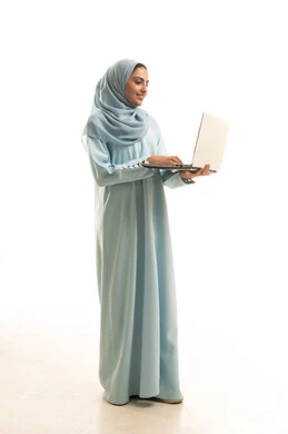 إنجاز المهام المطلوبة عبر اللابتوب، ادارة العمل عن بعد، استخدام جهاز تقني حديث ومتطور، بورتريه لامرأة عربية خليجية سعودية محجبة ترتدي العباءة تعمل على جهاز الحاسوب المحمول, الجسم بالطول الكامل، خلفية بيضاء