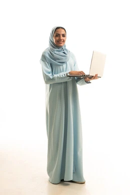 النظر للكاميرا بتعابير السرور، إنجاز المهام المطلوبة عبر اللابتوب، ادارة العمل عن بعد، استخدام جهاز تقني حديث ومتطور، بورتريه لامرأة عربية خليجية سعودية محجبة ترتدي العباءة تعمل على جهاز الحاسوب المحمول, الجسم بالطول الكامل، خلفية بيضاء