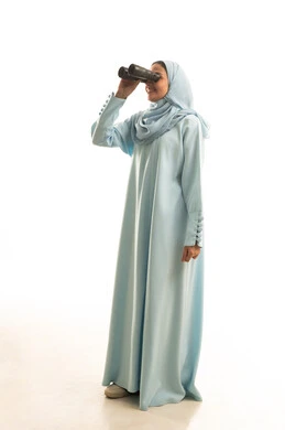 Seeing distant things through a telescope, future planning for goals and ambitions, a portrait of a Saudi Arabian Gulf woman wearing a black abaya, looking through a telescope with gestures of happiness and joy, full-body, white background.