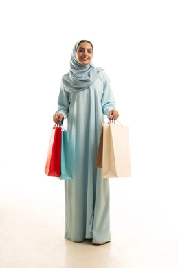 Looking with gestures of joy and happiness, getting offers and discounts, shopping and buying necessities and gifts, a portrait of a Saudi Gulf Arab woman wearing an abaya and hijab carrying shopping bags in her hands, a full-body image, white background.