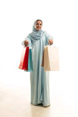 التسوق و شراء المستلزمات و الهدايا , الحصول على العروض و الحسومات , بورتريه لامرأة عربية خليجية سعودية ترتدي العباءة و الحجاب تحمل أكياس المشتريات بيديها , النظر بإيماءات الفرح و السرور , صورة للجسم بالطول الكامل , خلفية بيضاء