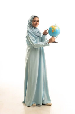 البحث والإستكشاف حول العالم، بورتريه لامرأة عربية سعودية خليجية ترتدي العباءة و الحجاب تمسك بيديها مجسم الكرة الارضية و تشير اليه، الجسم بالطول الكامل، خلفية بيضاء