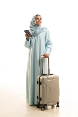 The feeling of joy in the advanced services of tourism and travel programs, the use of devices, technologies, and tourism applications, a portrait of a Saudi Arabian Gulf woman wearing a hijab and an abaya, holding a travel bag and a mobile phone in her hand, looking with gestures of happiness, full-body image, white background.