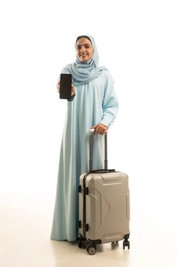 عرض شاشة سوداء فارغة عبر الهاتف المحمول، الذهاب في رحلة سفر، بورتريه لامرأة عربية خليجية سعودية ترتدي العباءة و الحجاب تمسك بيديها الجوال و حقيبة السفر، الجسم بالطول الكامل، خلفية بيضاء