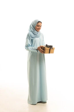 Expressing love and appreciation, celebrating birthdays, giving gifts on happy occasions, looking with gestures of happiness and joy, a portrait of a Saudi Arabian Gulf woman wearing a hijab and an abaya holding a gift box in her hands, full-body, white background.