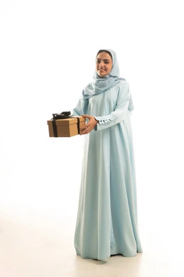 Gift giving on happy occasions, celebrating birthdays, expressing love and appreciation, looking with gestures of happiness and joy, a portrait of a Saudi Arabian Gulf woman wearing a hijab and an abaya holding a gift box in her hands, full body, white background.