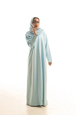 ايماءات التفاجوء والذهول ،الفحص والإستكشاف والقراءة، مفهوم توضيح الصورة، بورتريه  لشابة عربية خليجية سعودية محجبة ترتدي العباءة تنظر من خلال العدسة المكبرة، التدقيق والتركيز وتكبير الاشياء, أدوات بصرية للرؤية عن قرب، الجسم بالطول الكامل، خلفية بيضاء