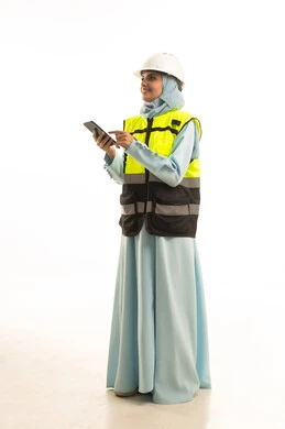 الإعمار بسواعد أبناء الوطن، استخدام التقنيات والتكنولوجيا الحديثة في القطاع الهندسي، مفهوم الهندسة والانشاءات المعمارية، بورتريه لمهندسة عربية خليجية سعودية ترتدي خوذة وسترة الحماية تقوم بتصفح الجوال ، الجسم بالطول الكامل، خلفية بيضاء