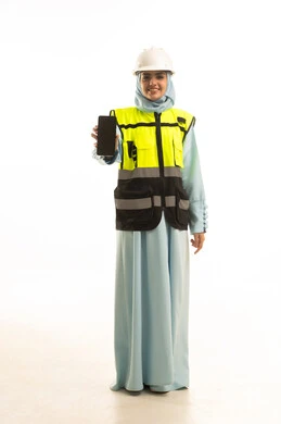 عرض شاشة سوداء فارغة عبر الهاتف المحمول, ايماءات تدل على السعادة والفرح, بورتريه لمهندسة عربية سعودية خليجية سعودية مبتسمة ترتدي العباءة و الخوذة و سترة الحماية تمسك بيديها الجوال ،مخططات وتصاميم هندسية، الجسم بالطول الكامل ، خلفية بيضاء