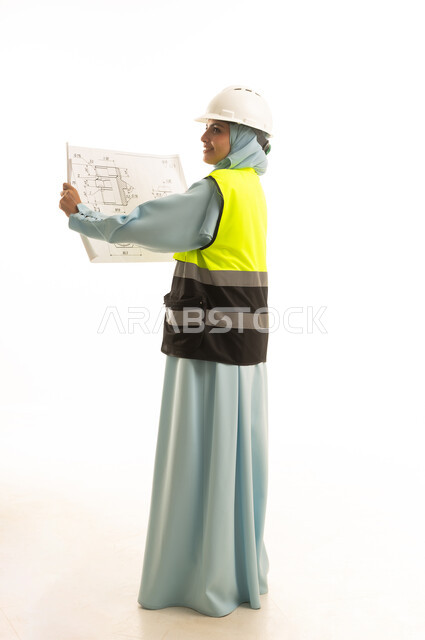 الإشراف على مخططات المشاريع الهندسية، العمل في مجال الهندسة، مفهوم الانشاءات المعمارية، بورتريه من الخلف لمهندسة معمارية عربية سعودية خليجية ترتدي العباءة و ستره و خوذة الحماية تحمل بيدها مخطط البناء، مهنة ووظيفة نسائية في المملكة العربية السعودية، خلفية بيضاء