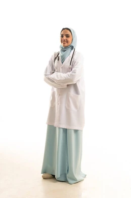 تحقيق الطموح والوقوف بثقة, بورتريه لطبيبة عربية خليجية سعودية مبتسمة ترتدي المعطف الطبي الأبيض وسماعة الفحص تقف بأيدي متقاطعة وتنظرالى الكاميرا بتعابير السرور، تقديم الخدمات والمساعدة الطبية, العمل في المستشفيات والمراكز الصحية, الجسم بالطول الكامل، خلفية بيضاء