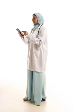 تقديم الخدمات للمرضى بكل كفاءه, اجراء الاستشارات الطبيه عن بعد, استخدام الجوال في البحث والتطوير، بورتريه لطبيبة عربية خليجية سعودية ترتدي المعطف الابيض تستخدم الهاتف المحمول ، الجسم بالطول الكامل، خلفية بيضاء