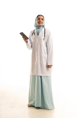 النظر الى شيء ما ، تقديم الخدمات للمرضى بكل كفاءه, اجراء الاستشارات الطبيه عن بعد, استخدام الجوال في البحث والتطوير، بورتريه لطبيبة عربية خليجية سعودية ترتدي المعطف الابيض تستخدم الهاتف المحمول ، الجسم بالطول الكامل، خلفية بيضاء