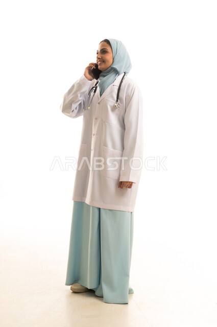 Providing remote consultation to patients via mobile, a portrait of a Saudi Gulf Arab woman wearing a hijab and a medical coat making a phone call on a mobile phone, using modern technology, full-body, white background.