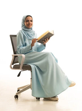 النظر للكاميرا بتعابير السرور، قضاء الوقت بالقراءة والتعلم والثقافة، مفهوم التعلم الذاتي، بورتريه لامراة عربيه خليجيه سعودية ترتدي العباءة و الحجاب تجلس على كرسي تقوم بمطالعة كتاب، خلفية بيضاء