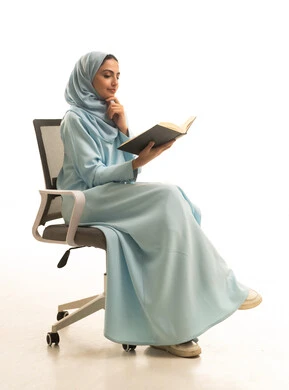 مفهوم التعلم الذاتي، ايماءات التمعن والتركيز، قضاء الوقت بالقراءة والتعلم والثقافة، بورتريه لامراة عربيه خليجيه سعودية ترتدي العباءة و الحجاب تجلس على كرسي تقوم بمطالعة كتاب، خلفية بيضاء
