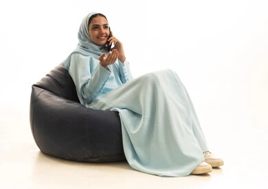 اجراء مكالمة هاتفية عبر الجوال، الدردشة مع الاهل و الاصدقاء، بورتريه لامراة عربية خليجية سعودية ترتدي الحجاب والعباءة تجلس على كرسي بين باج تحمل بيدها الهاتف المحمول ، استخدام الأجهزة التقنية الحديثة، خلفية بيضاء