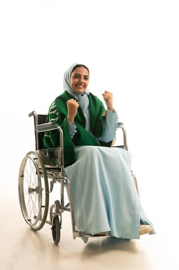 الانتصار والفوز والنجاح، مفهوم الانجاز وتحقيق الاهداف، اليوم الوطني السعودي 23 سبتمبر، بورتريه لشابة عربية سعودية خليجية من ذوي الاحتياجات الخاصة ترتدي العباءه و علم السعودية تجلس على كرسي متحرك ترفع يدها بإيماءات الحماس لفوز وانتصار الفريق المفضل، خلفية بيضاء