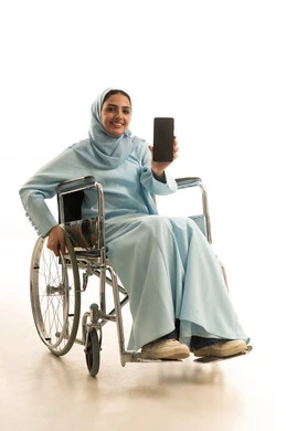 عرض تطبيقات الهاتف المحمول، التسويق الالكتروني باستخدام التقنية والتكنولوجيا، بورتريه لامراه عربية خليجية سعودية من ذوي الاحتياجات الخاصة محجبة ترتدي العباءة تجلس على كرسي متحرك تحمل بيدها جوال بشاشة سوداء فارغة، خلفية بيضاء