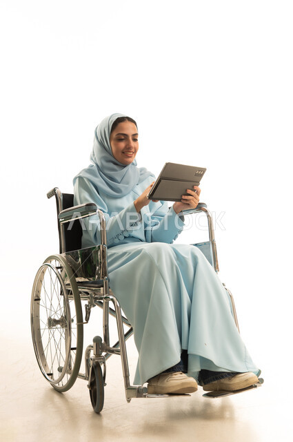 Tapping on the tablet screen, making video calls and live broadcasts, e-learning through the use of modern technologies, following favorite movies and series online, a portrait of a Saudi Gulf Arab woman with special needs wearing a hijab and an abaya sitting in a wheelchair holding a portable tablet, white background.