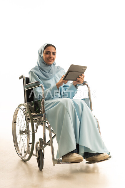 Making video calls and live broadcasts, e-learning through the use of modern technologies, following favorite movies and series online, tapping on the tablet screen, a portrait of a Saudi Gulf Arab woman with special needs wearing a hijab and an abaya sitting in a wheelchair holding a mobile tablet, white background.