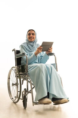 التعلم الإلكتروني من خلال استخدام التقنيات الحديثة، إجراء مكالمات الفيديو والبثوث المباشرة، متابعة الأفلام والمسلسلات المفضلة عبر الإنترنت، النقر على شاشة الجهاز اللوحي، بورتريه لامراه عربية خليجية سعودية من ذوي الاحتياجات الخاصة محجبة ترتدي العباءة تجلس على كرسي متحرك تحمل جهاز التابلت المحمول، خلفية بيضاء